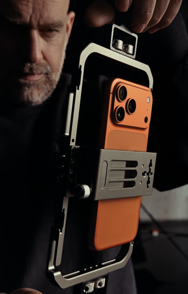 Close-up of a man adjusting iPhone 17 Pro attached to a gimbal, as if framing an action shot or recording a video, to demonstrate how iPhone 17 captures striking detail at close range.