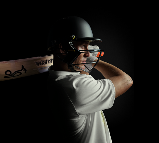 Close-up of cricketer Marnus Labuschagne wearing a cricket helmet and looking ahead with his arm swung to the left, cricket bat held over his shoulder. Shot in low-light against a black background for dramatic effect.