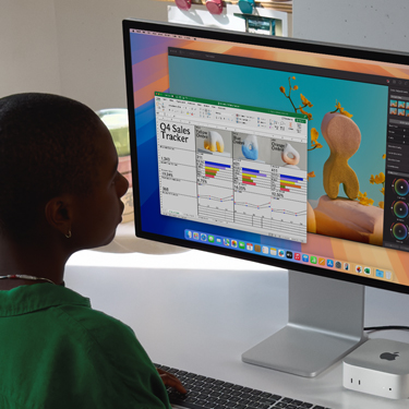 Una mujer trabaja en una hoja de cálculo de Excel en un Mac, sentada en una mesa de trabajo. La hoja de cálculo de Excel es un registro de las ventas del cuarto trimestre. Detrás de la ventana con la hoja de cálculo de Excel hay una ventana de Pixelmator Pro.