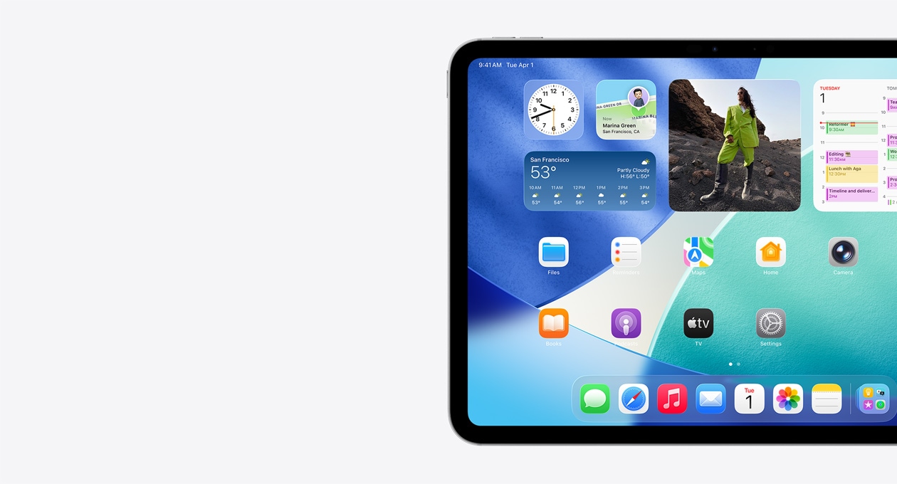 iPad, orientace na šířku, pouze levá strana obrazovky, plocha s widgety včetně průhledných hodin s efektem Liquid Glass, aplikace Najít, widgetu Počasí, dvou řádků menších aplikací a Docku