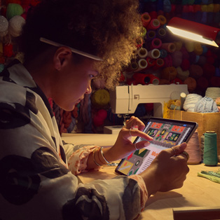 A person sitting at a desk uses two fingers on the screen of an iPad to zoom in on an image.