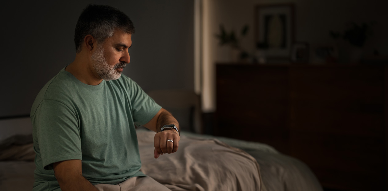 Un hombre sentado en la cama consulta su Apple Watch.