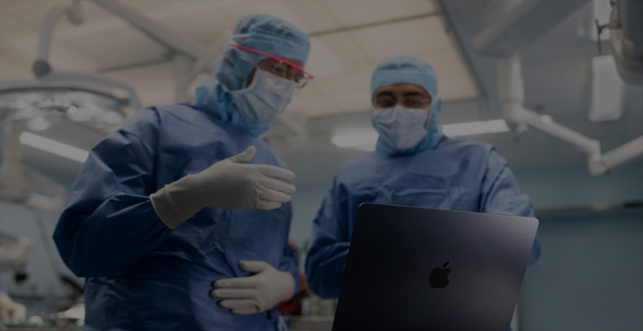Dos médicos de uniforme miran un MacBook Pro en un quirófano.