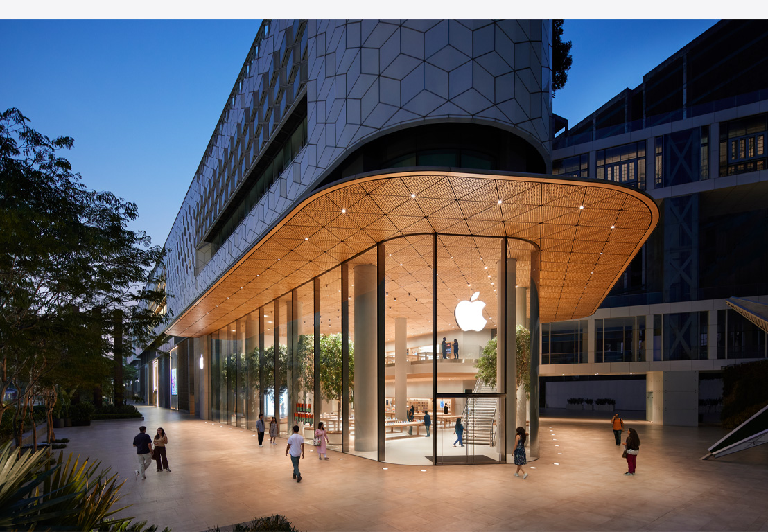 Apple Store vào ban đêm, cửa sổ bằng kính, đèn sáng bên trong, logo Apple nằm ở giữa phía trên cùng của cửa chính.