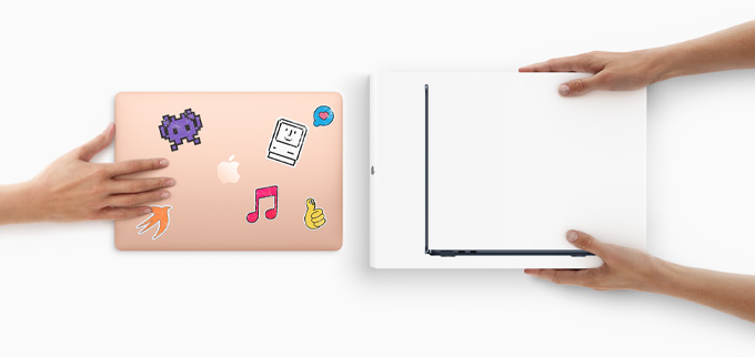 A hand slides a MacBook with stickers on the cover toward two hands holding a new MacBook in the box