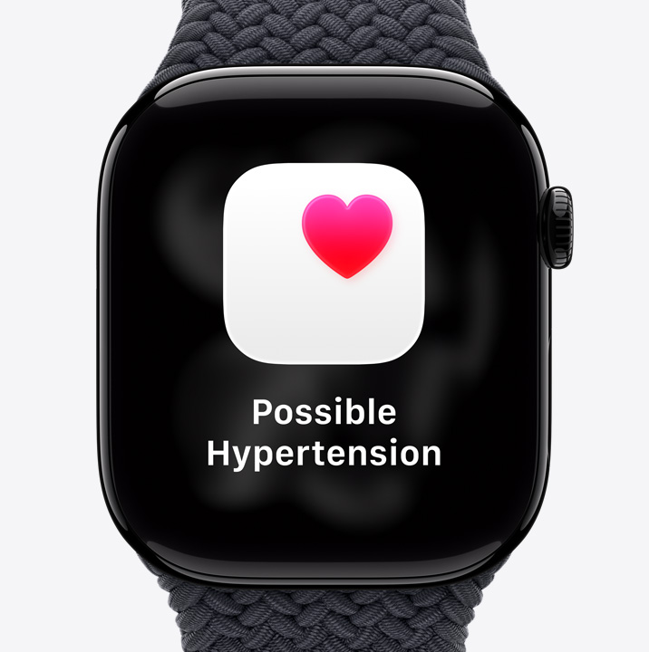 Apple Watch Series 11, alumiinikuori, värinä kiillotettu peilimusta, mahdollisesti kohonneen verenpaineen ilmoitus, pinkki sydän valkoisessa laatikossa, näkymä oikeasta sivusta, Digital Crown, musta urheiluranneke